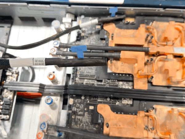 Side-by-side videos of a server tray: cables and copper components on the left, and a robotic gripper above a connector outlined in yellow on the right. 