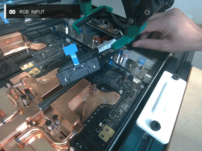Side-by-side videos of a server tray: cables and copper components on the left, and a robotic gripper above a connector outlined in yellow on the right. 